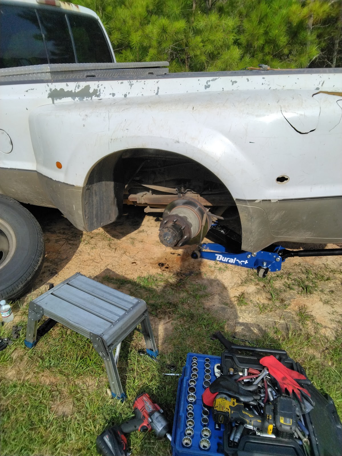 Robert's Mobile Services — white Ford F-350 dually with rear wheel removed on a blue Duralast jack in a dirt driveway, DeWalt socket set staged