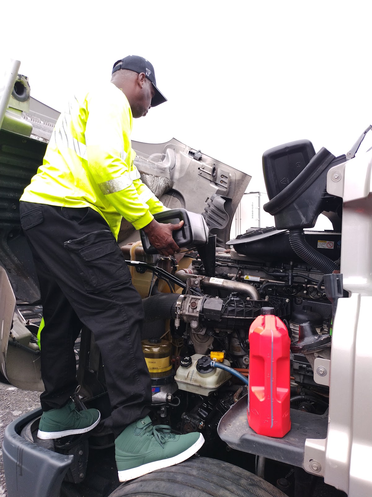 Robert's Mobile Services — Robert in a yellow high-vis long-sleeve on the step of a commercial box truck pouring oil into the engine bay