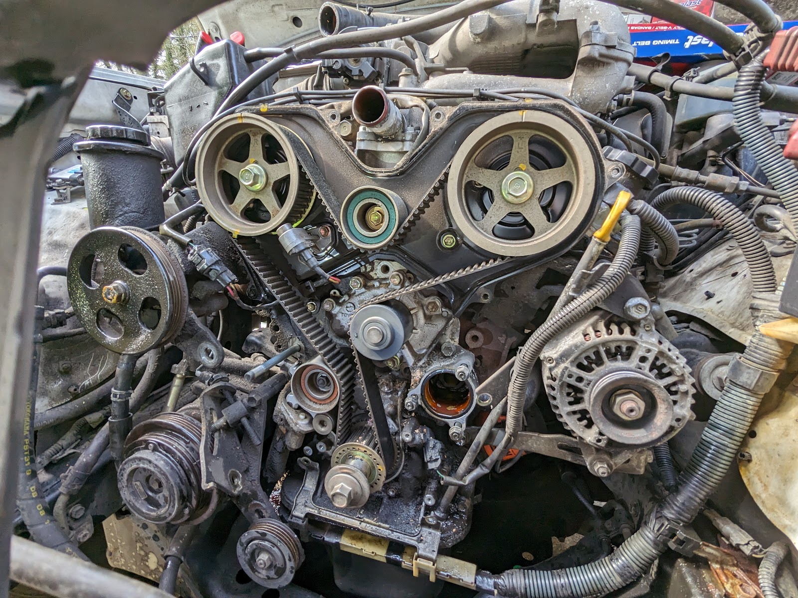 Robert's Mobile Services — V6 engine timing cover removed exposing belts, pulleys, and alternator for a major timing-belt job